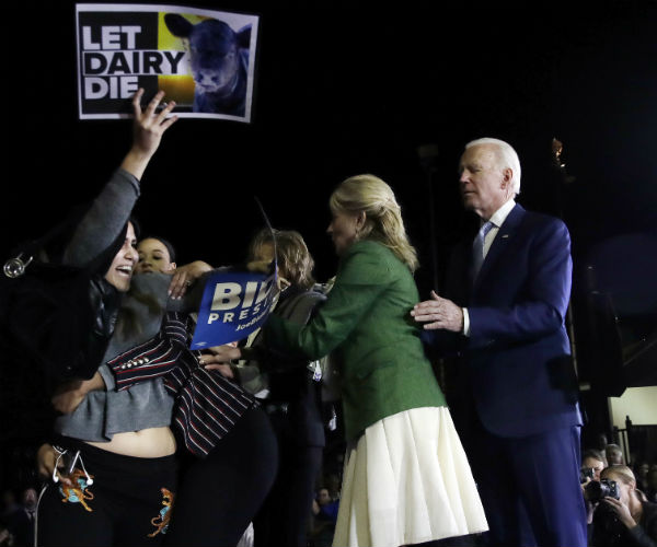 a protester, at left, holding up a 'let dairy die' sign is held back by jill biden and adviser symone sanders 