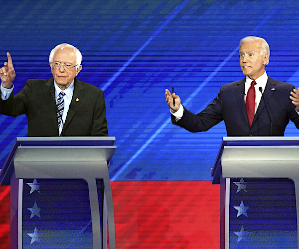 bernie sanders raises his hand while joe biden exults during a democratic presidential primary debate